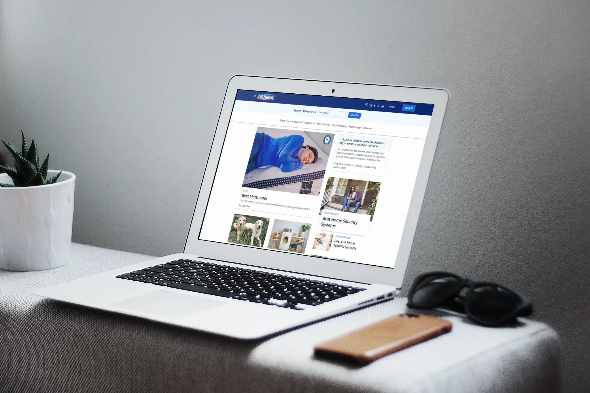 The redesigned U.S. News 360 homepage shown on a laptop, with a large featured mattress review, a supporting home security recommendation, and category links along the top.